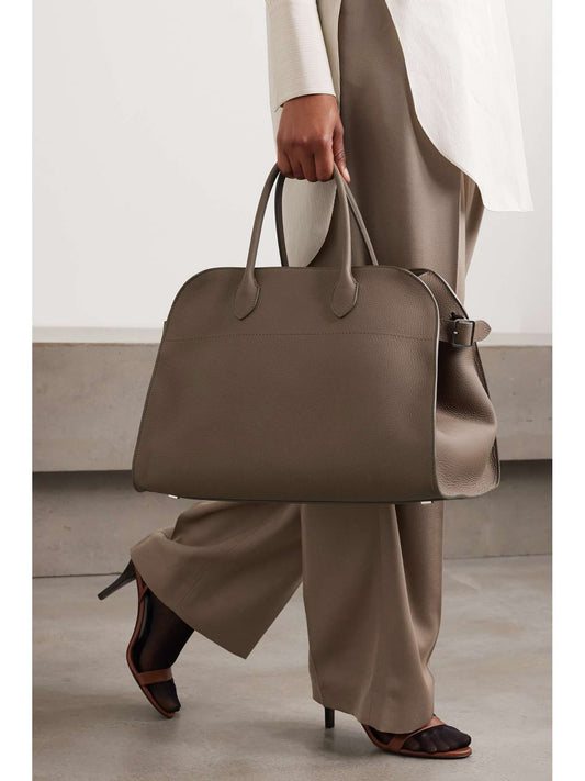 Stylish person holding The Row Margaux investment bag in elegant taupe, paired with chic beige outfit.