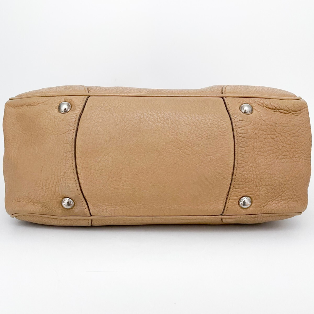 Bunden af Prada tote – metalbeskyttelse og slidrammer i beige læder.