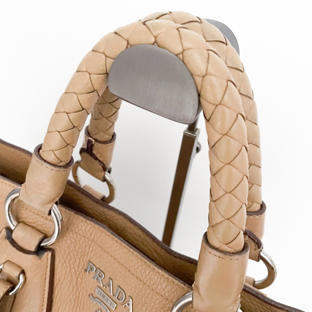 Nærbillede af flet-håndtag og sølv hardware på Prada tote i beige læder.