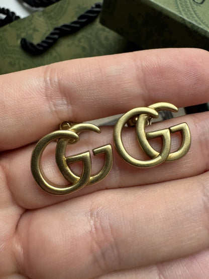 Close-up af Gucci GG Marmont logo øreringe i antikguld med korrekt proportion og finish